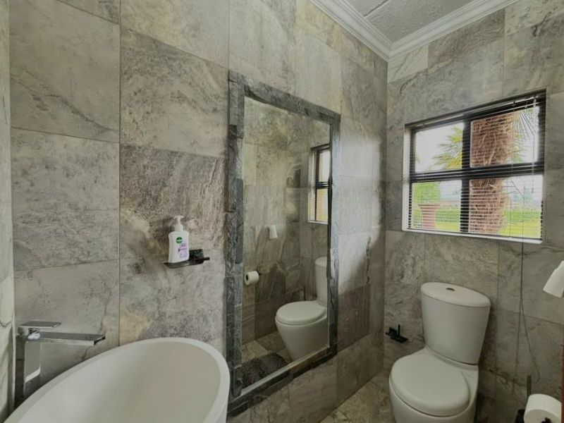A modern bathroom featuring stone wall tiling, a sleek freestanding basin with wall-mounted mixer, and a contemporary toilet.
