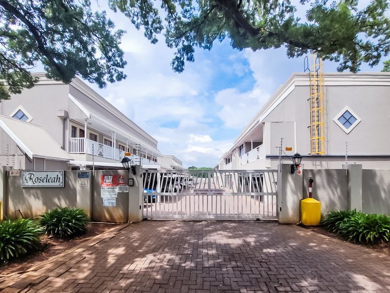 Front entrance view of the Rosleah apartment complex, featuring a secure gated driveway, paved access, and well-maintained building facades with balconies.