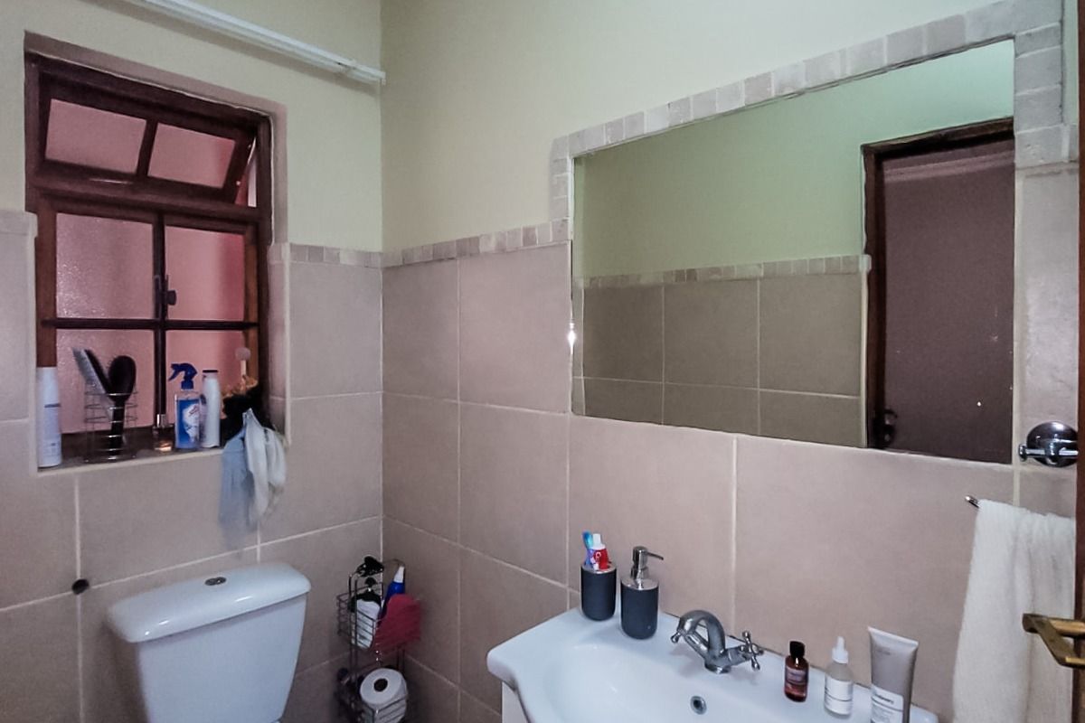 A functional bathroom featuring a vanity cabinet with basin, wall-mounted mirror, ceramic tiling, and a standard toilet.