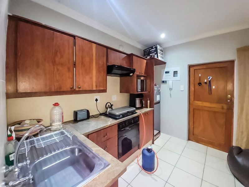 A functional kitchen featuring wooden cabinetry, a stainless steel sink, built-in oven with extractor fan, and tiled flooring.