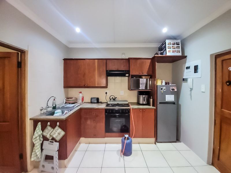 A functional kitchen featuring wooden cabinetry, built-in oven, gas hob, extractor fan, and tiled flooring.