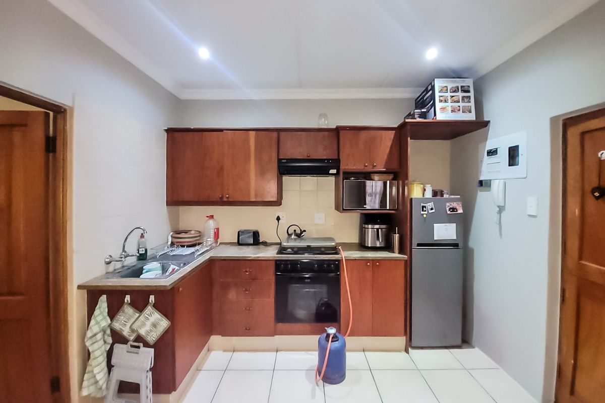 A functional kitchen featuring wooden cabinetry, built-in oven, gas hob, extractor fan, and tiled flooring.