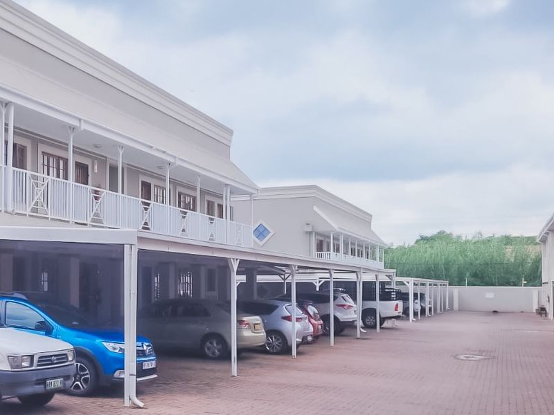 Exterior view of an apartment complex featuring covered parking bays and upper-level balconies with metal railings.