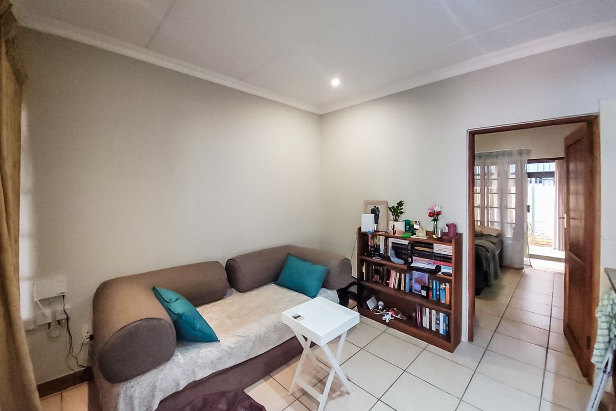 A living room area featuring ceramic floor tiles, recessed downlighting, and coved ceiling cornices, with a doorway leading to an adjacent room.