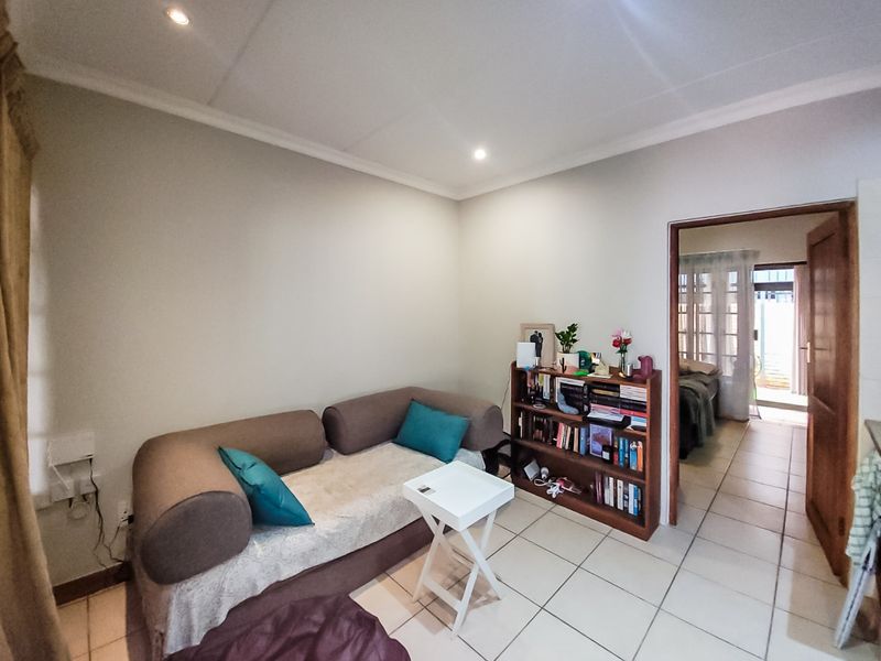 A living room area featuring ceramic floor tiles, recessed downlighting, and coved ceiling cornices, with a doorway leading to an adjacent room.