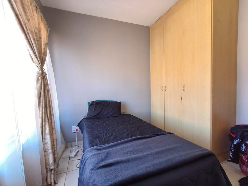 A functional bedroom featuring neutral wall tones, tiled flooring, and a large built-in wooden wardrobe providing ample storage space.