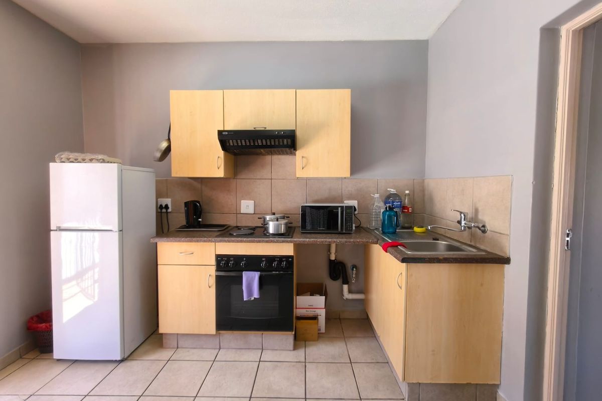 A functional kitchen featuring light wood cabinetry, tiled backsplash, built-in oven and hob, and a stainless steel sink with exposed plumbing.