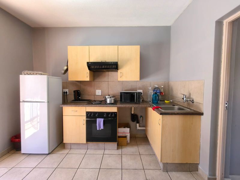 A functional kitchen featuring light wood cabinetry, tiled backsplash, built-in oven and hob, and a stainless steel sink with exposed plumbing.