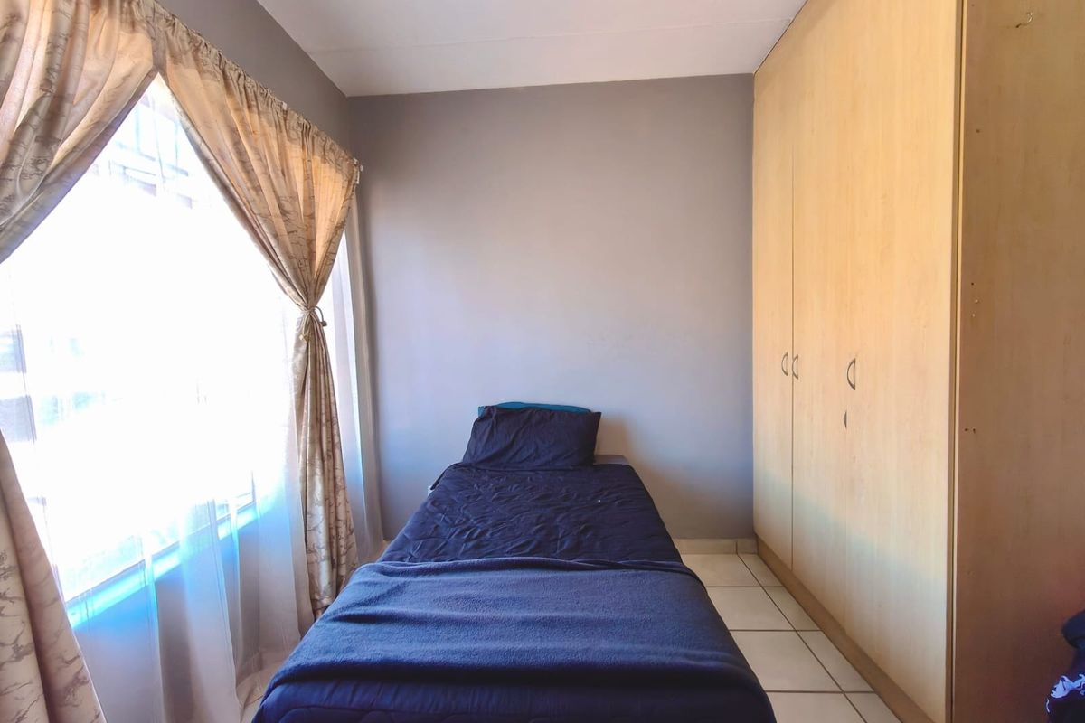 A functional bedroom featuring built-in wooden cupboards and tiled flooring, offering a simple and practical living space.