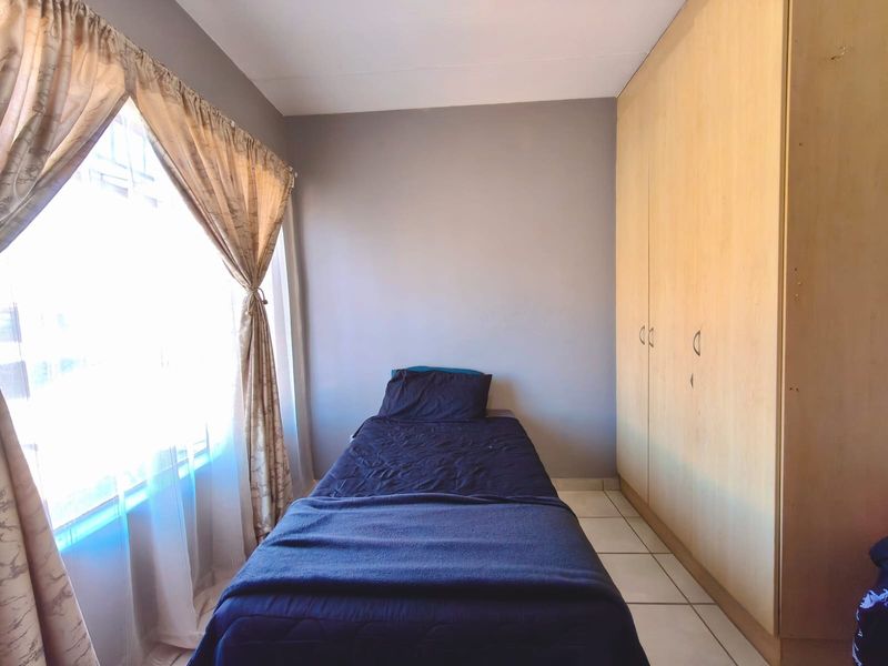 A functional bedroom featuring built-in wooden cupboards and tiled flooring, offering a simple and practical living space.