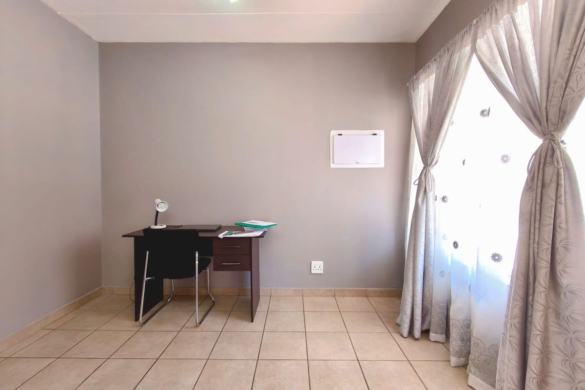 A functional office space featuring neutral wall tones, tiled flooring, and natural light through a large window.