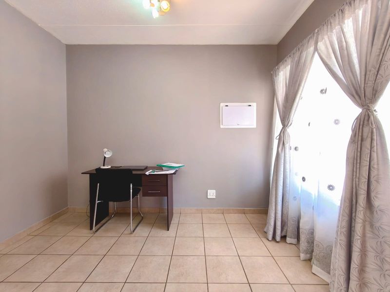 A functional office space featuring neutral wall tones, tiled flooring, and natural light through a large window.