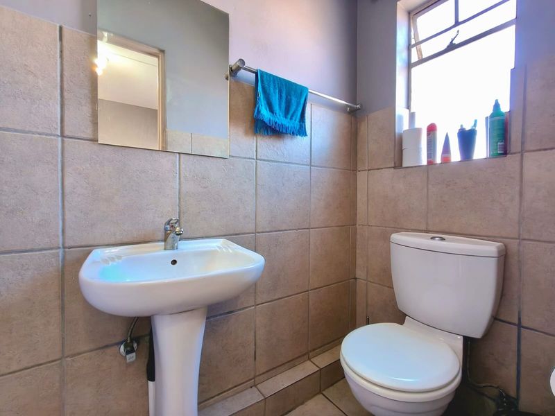 A functional bathroom featuring a pedestal basin, toilet, and neutral wall tiling, providing a clean and practical space.