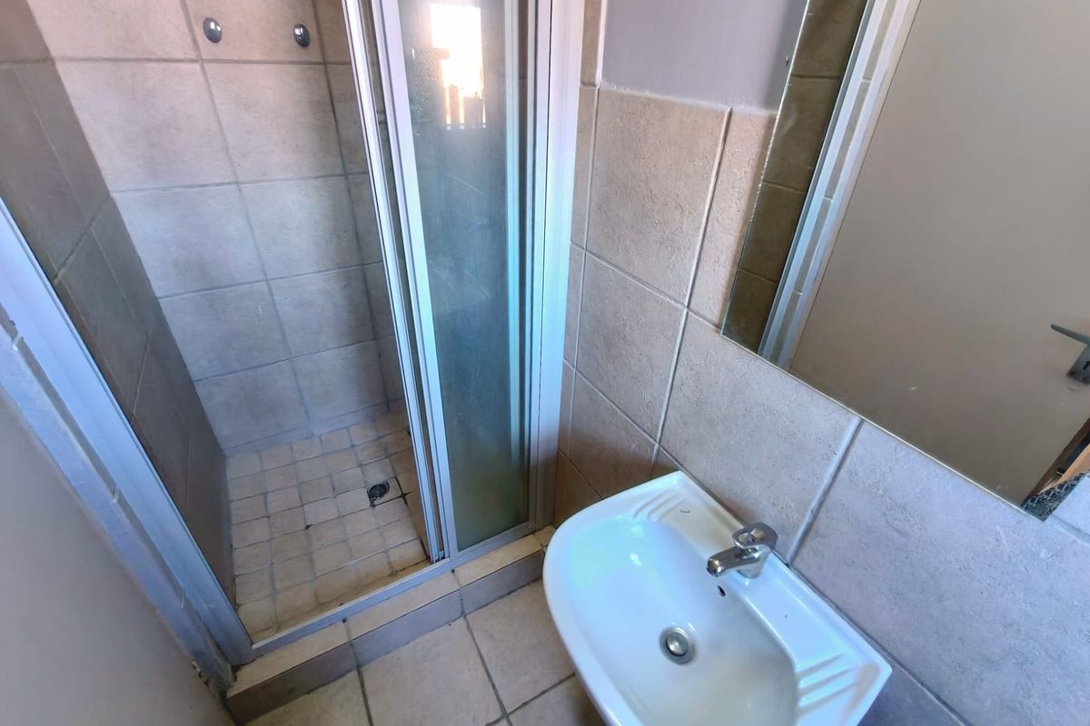 A functional bathroom featuring a shower enclosure, pedestal basin, and wall-mounted mirror with neutral ceramic tiling throughout.