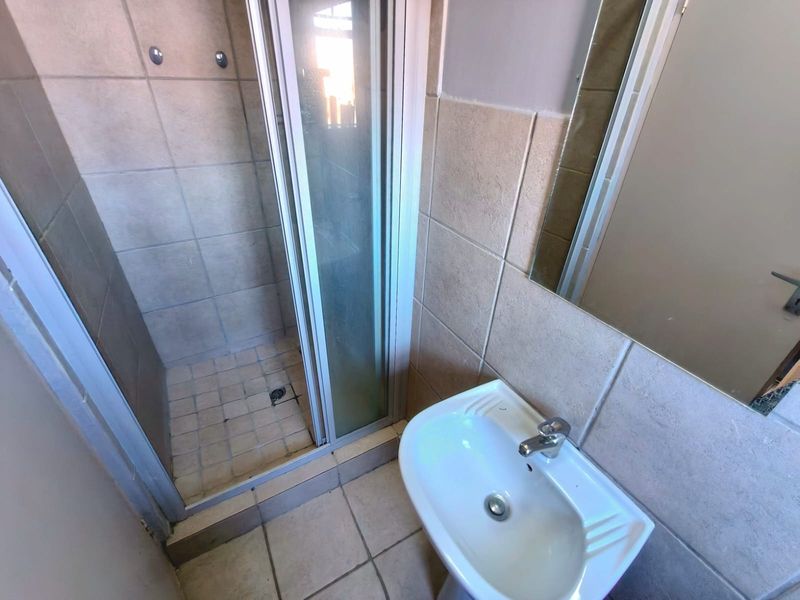 A functional bathroom featuring a shower enclosure, pedestal basin, and wall-mounted mirror with neutral ceramic tiling throughout.