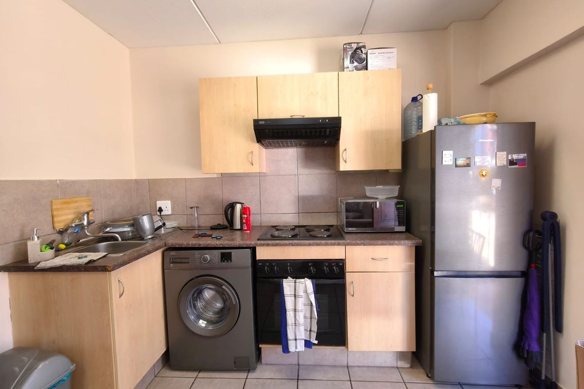 Compact kitchen featuring light wood-finish cabinetry, tiled backsplash, built-in oven with hob, extractor fan, and integrated washing machine.