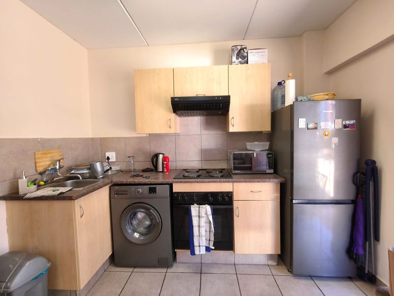 Compact kitchen featuring light wood-finish cabinetry, tiled backsplash, built-in oven with hob, extractor fan, and integrated washing machine.