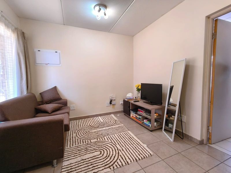 A compact living room featuring neutral walls, tiled flooring, and a ceiling light fixture, providing a functional and well-lit space.