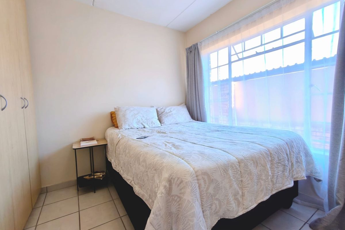 A functional bedroom featuring tiled flooring and a built-in wardrobe, illuminated by natural light from a large window.