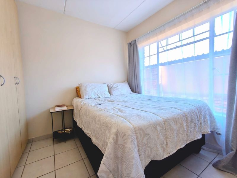 A functional bedroom featuring tiled flooring and a built-in wardrobe, illuminated by natural light from a large window.