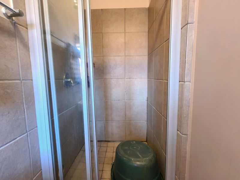 A compact shower stall featuring tiled walls and flooring, currently showing signs of wear and requiring maintenance or cosmetic updates.
