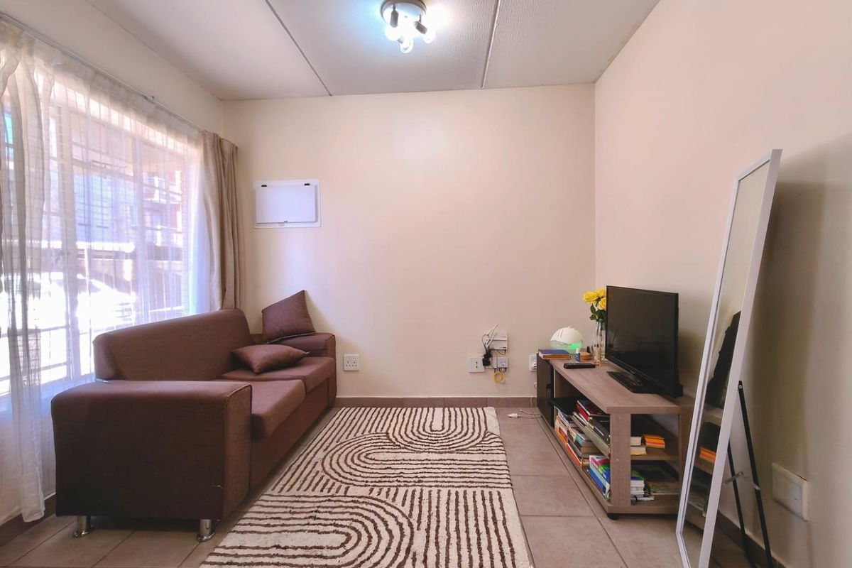A functional living room featuring tiled flooring, neutral walls, and natural light from a large window.