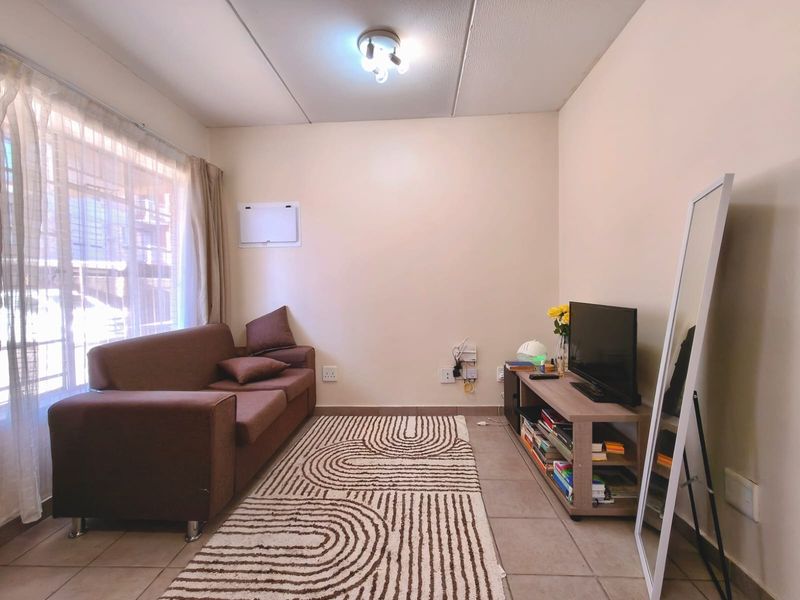 A functional living room featuring tiled flooring, neutral walls, and natural light from a large window.