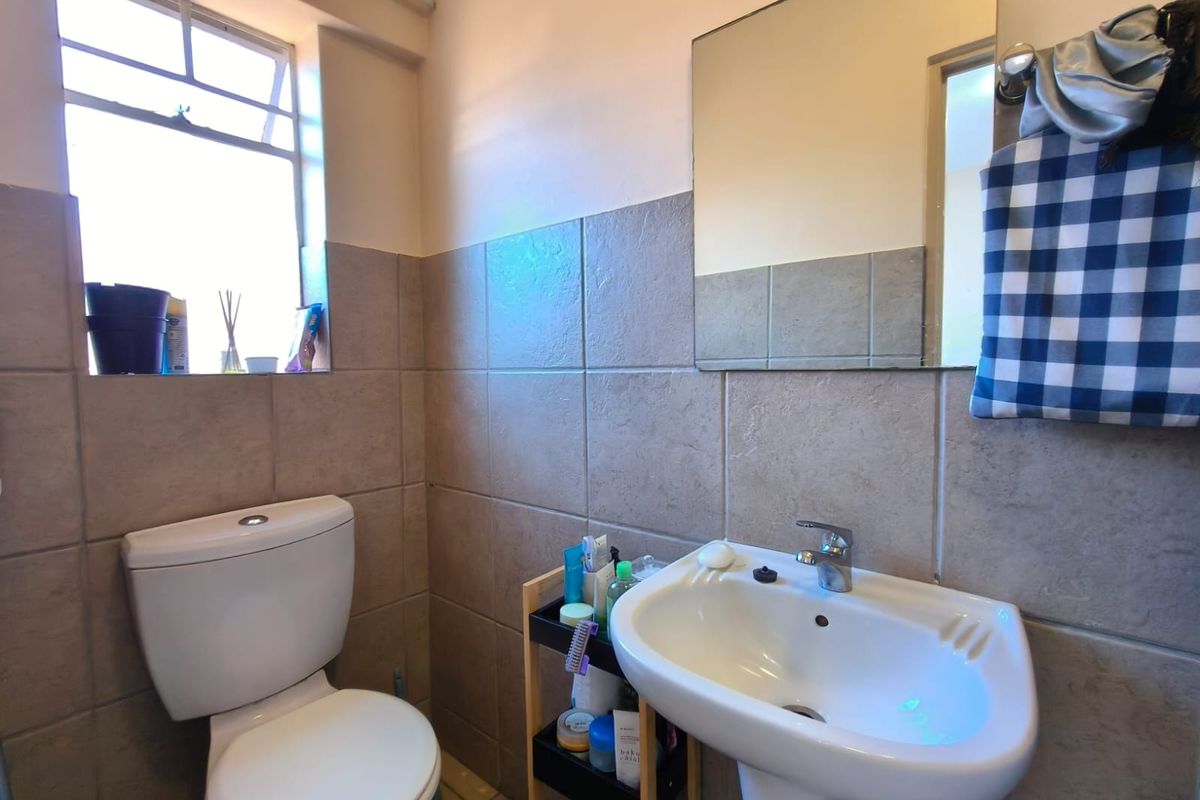 A functional bathroom featuring a pedestal basin, toilet, and neutral wall tiling with natural light from a casement window.