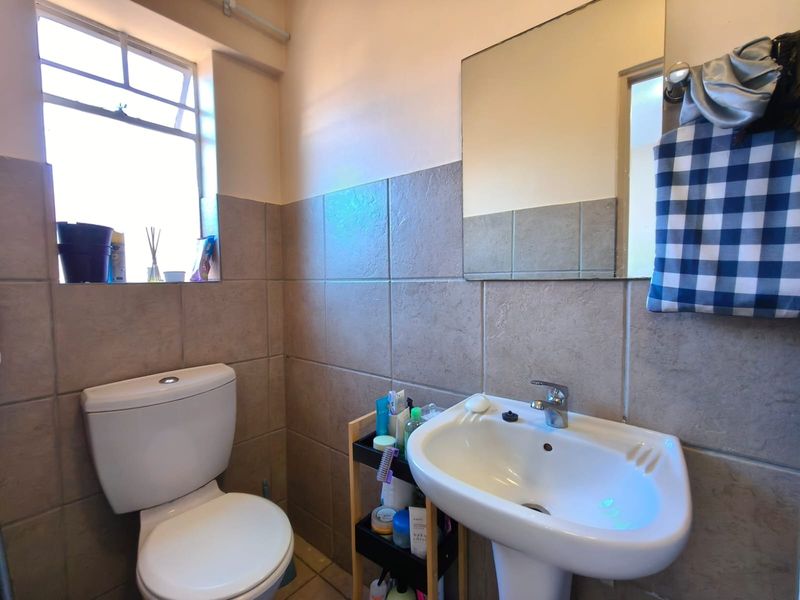 A functional bathroom featuring a pedestal basin, toilet, and neutral wall tiling with natural light from a casement window.