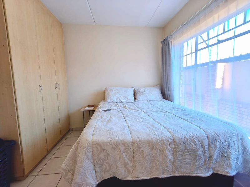 A functional bedroom featuring built-in wooden cupboards and tiled flooring, with natural light entering through a large window.