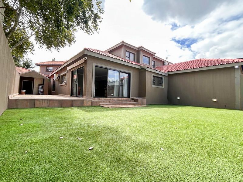 Rear view of the house featuring a paved patio area, sliding glass doors, and a well-maintained artificial lawn.