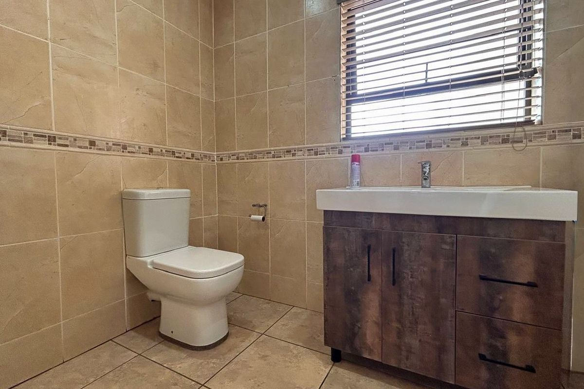 A clean and functional bathroom featuring neutral ceramic wall and floor tiles, a modern vanity cabinet with a basin, and a standard toilet.