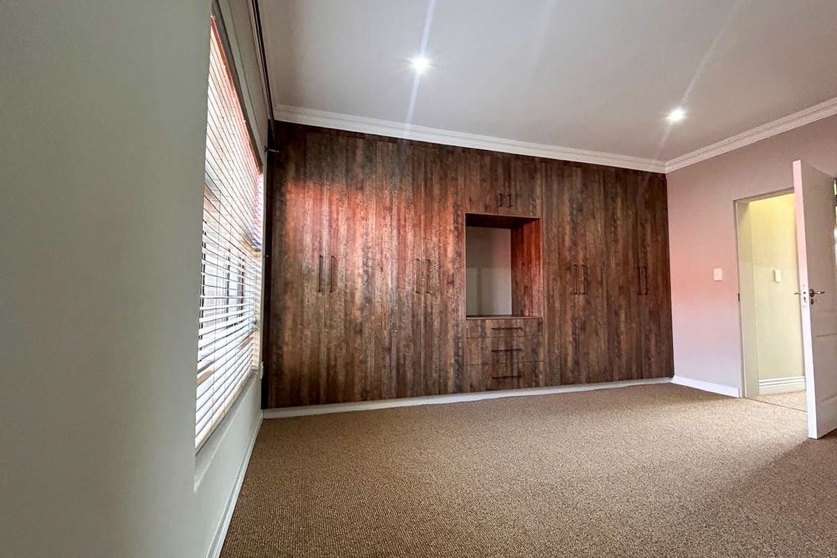A spacious bedroom featuring extensive built-in wooden cabinetry, neutral carpeting, recessed lighting, and venetian blinds.