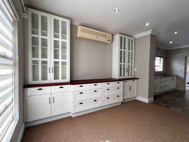 A bright living area featuring extensive built-in white cabinetry with dark countertops, recessed lighting, and a wall-mounted air conditioning unit.
