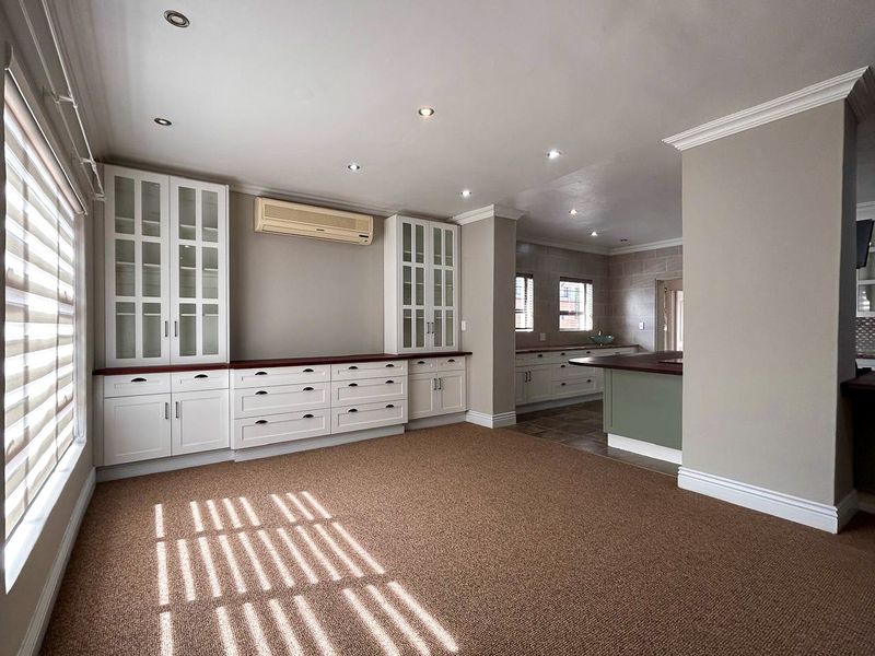 Spacious open-plan living and kitchen area featuring extensive built-in cabinetry, recessed lighting, and a seamless transition between carpeted and tiled flooring zones.