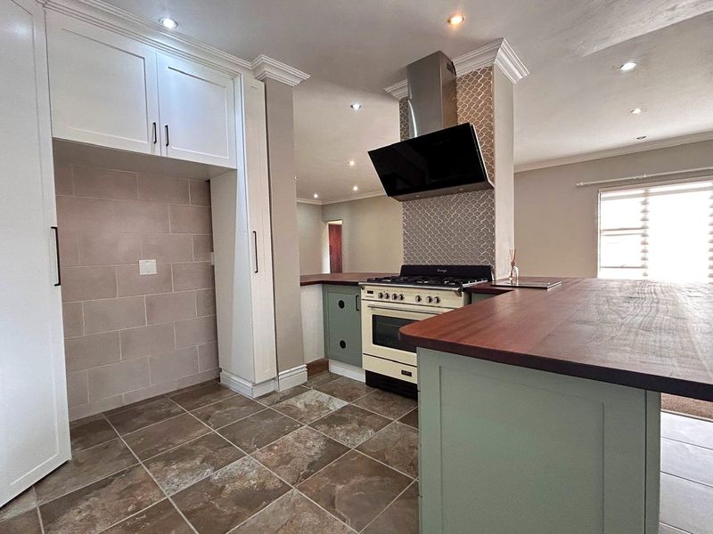 Modern kitchen featuring a gas stove, extractor fan, wooden countertops, and ample built-in cabinetry with a stylish tiled backsplash.