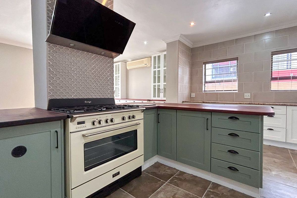 A well-maintained kitchen featuring sage green cabinetry, a vintage-style gas stove with extractor fan, tiled flooring, and neutral wall tiling.