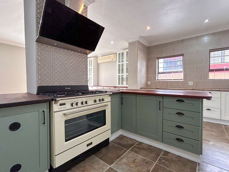 A well-maintained kitchen featuring sage green cabinetry, a vintage-style gas stove with extractor fan, tiled flooring, and neutral wall tiling.