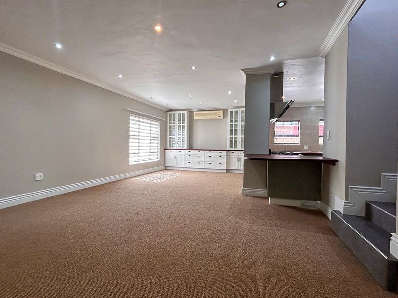 Spacious open-plan living area featuring built-in cabinetry, a breakfast bar, recessed lighting, and neutral carpeting, offering a versatile layout for modern living.