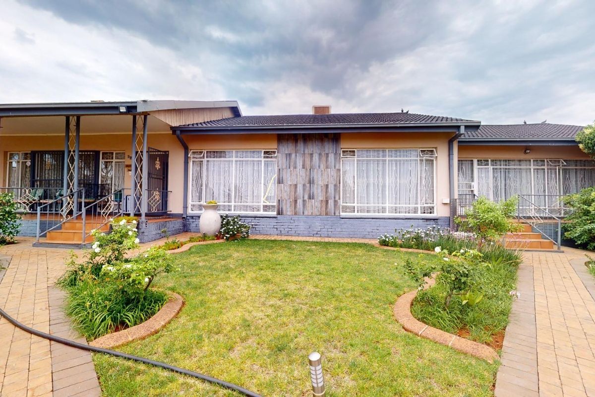 A well-maintained rear exterior view featuring a paved courtyard, landscaped garden beds, and a covered patio area with security gates.
