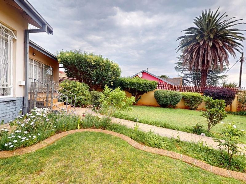A well-maintained rear garden featuring a paved walkway, established landscaping, and a brick boundary wall, providing a pleasant outdoor space.