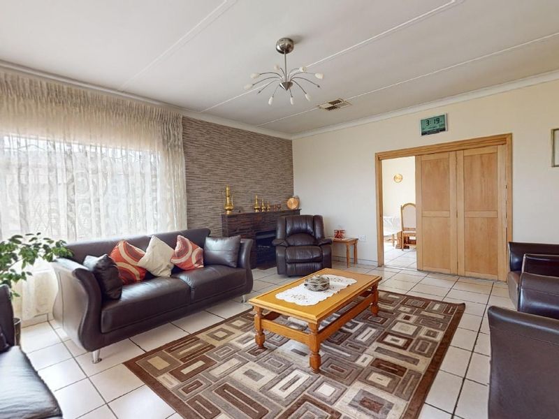 A spacious living room featuring tiled flooring, a textured feature wall, and sliding wooden doors leading to an adjacent room.