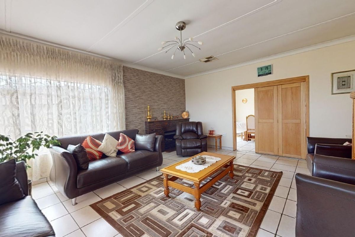 A spacious living room featuring tiled flooring, a textured feature wall, and sliding wooden doors leading to an adjacent room.