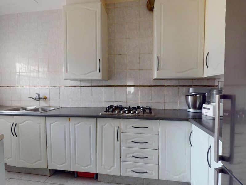 A functional kitchen featuring white cabinetry, a gas hob, and tiled backsplash, offering a classic layout with ample storage and counter space.