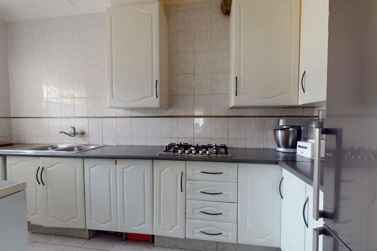 A functional kitchen featuring white cabinetry, a gas hob, and tiled backsplash, offering a classic layout with ample storage and counter space.