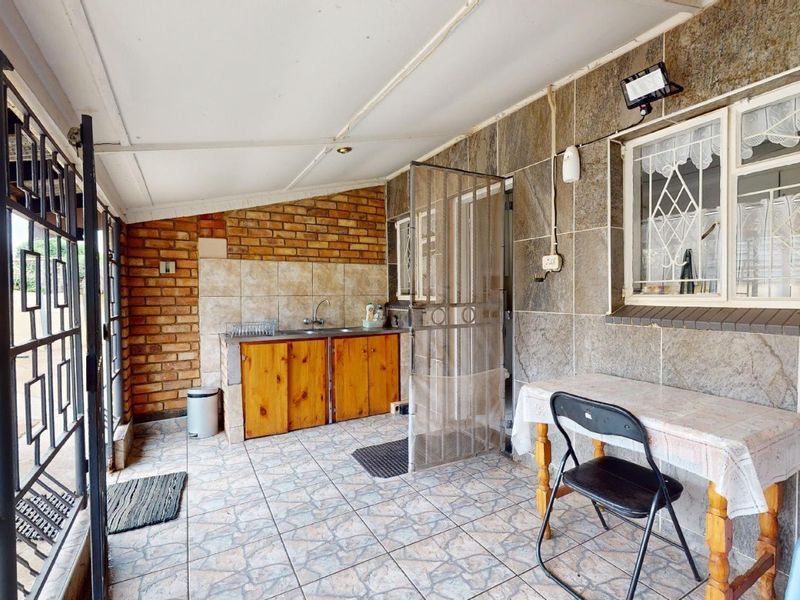Covered patio area featuring stone-clad walls, exposed brickwork, tiled flooring, and a built-in sink with wooden cabinetry, providing a functional outdoor utility space.