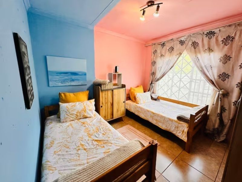 A bedroom featuring tiled flooring, security bars on the window, and a ceiling light fixture, currently configured with two single beds.
