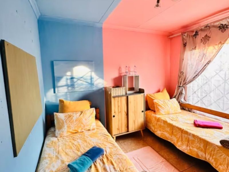 A bedroom featuring tiled flooring, security bars on the window, and a ceiling-mounted light fixture, currently configured with two single beds.