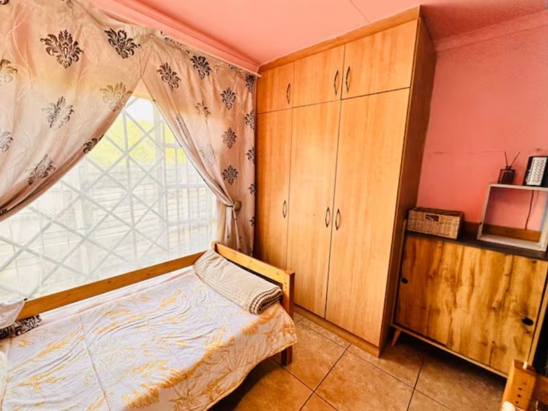 A bedroom featuring built-in wooden wardrobes, tiled flooring, and a window with security bars. The room requires cosmetic updates to the wall finishes.
