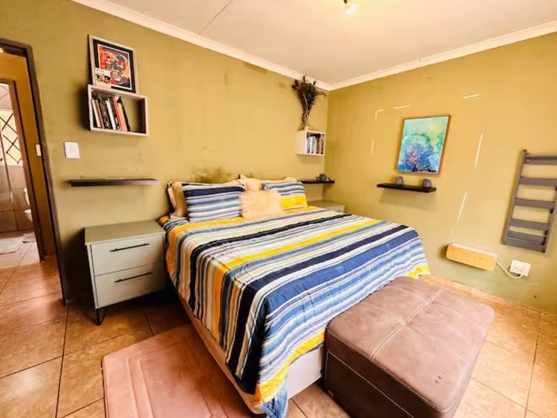 A bedroom featuring tiled flooring and direct access to an en-suite bathroom, with wall surfaces requiring cosmetic attention.